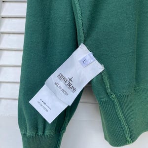 Pu&ograve; includere: Un maglione verde Stone Island con un'etichetta bianca che dice "Stone Island" e "Art. 581553788".