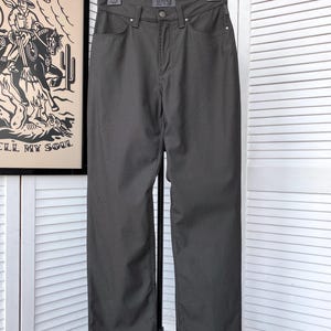 May include: Dark grey straight leg jeans with a black leather label that says "VERSACE JEANS COUTURE" hanging on a black hanger.