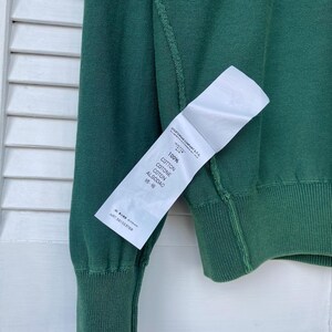 Pu&ograve; includere: Un maglione verde a maniche lunghe con un'etichetta bianca che recita "100% Cotone, Cotone, Coton, Algodao, 棉", e "ART. 5011532704".