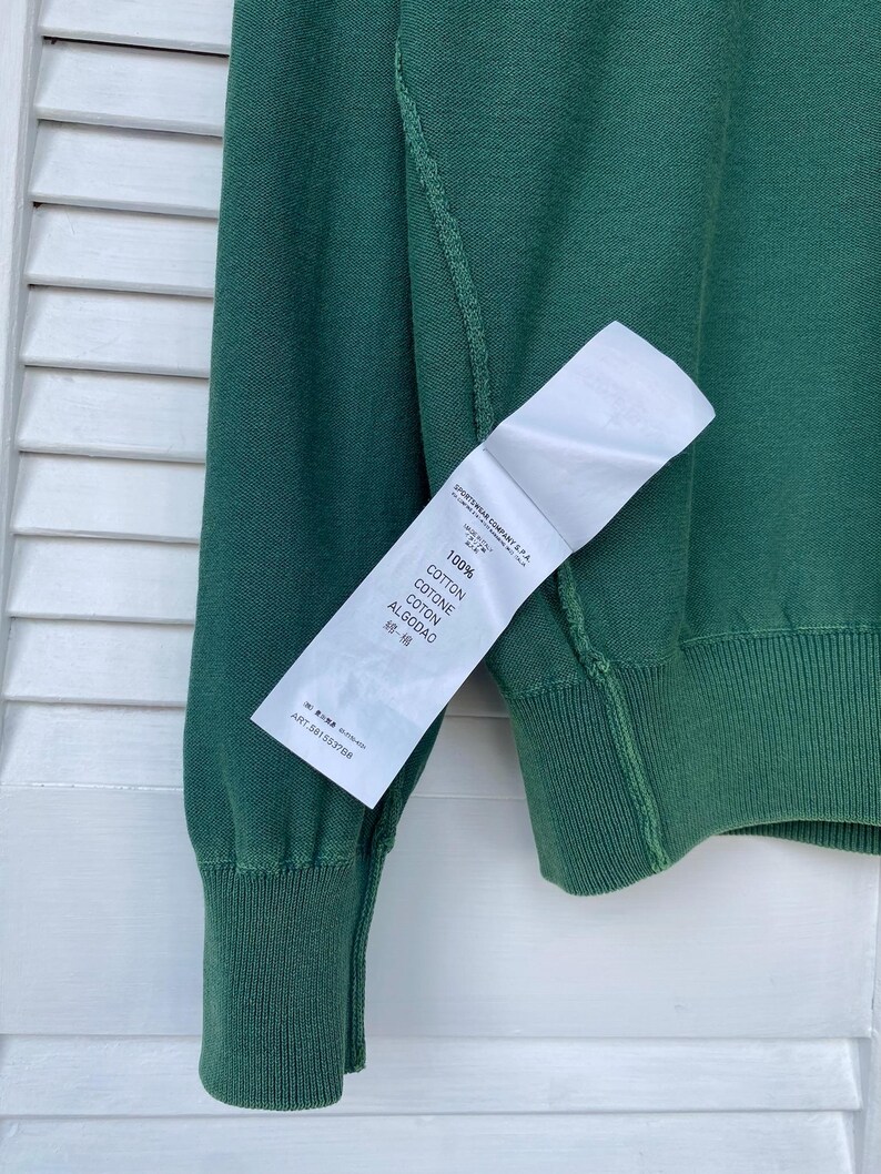 Pu&ograve; includere: Un maglione verde a maniche lunghe con un'etichetta bianca che recita "100% Cotone, Cotone, Coton, Algodao, 棉", e "ART. 5011532704".