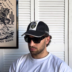 May include: A black and white baseball cap with the Juventus logo on the front. The cap has a curved brim and a white stripe across the top. The person is wearing black sunglasses and a white t-shirt with text that reads "PACK IT IN PACK IT OUT".