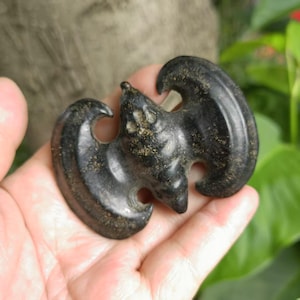 May include: A dark, carved bat pendant with a detailed design. The bat is black with gold flecks, and its wings are spread. The pendant is likely made of stone or a similar material. The bat is a symbol of good luck and prosperity.