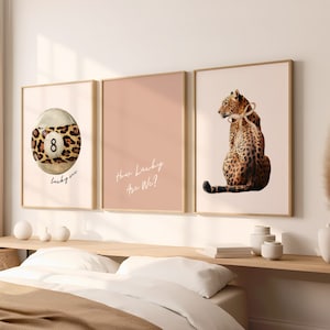 May include: Three framed prints with a pink background. The left print features a leopard print 8-ball with the text "lucky me". The centre print has the text "How Lucky Are We?" The right print features a leopard with a ribbon around its neck.