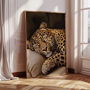 Pu&ograve; includere: Stampa artistica incorniciata raffigurante un leopardo addormentato. Il leopardo, con il suo manto maculato, riposa su un cuscino color crema. La cornice dorata contrasta con il muro bianco, creando un'atmosfera serena.