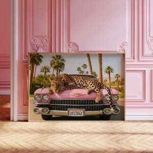 Puede incluir: Impresi&oacute;n enmarcada que presenta un leopardo descansando sobre un coche rosa vintage. El coche est&aacute; situado contra un fondo de palmeras y cielo azul. La matr&iacute;cula dice "2FLT842". La obra tiene un tema retro y tropical.