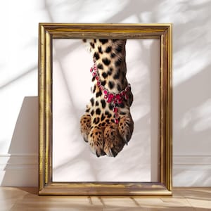 Könnte beinhalten: Nahaufnahme einer Leopardpfote, die ein rotes, mit Juwelen besetztes Armband trägt. Die Pfote ist scharf, der Hintergrund unscharf.