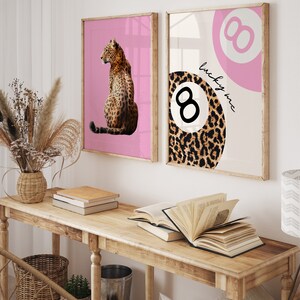 Puede incluir: Dos impresiones enmarcadas con fondo rosa. La impresi&oacute;n de la izquierda presenta un leopardo sentado sobre un fondo rosa. La impresi&oacute;n de la derecha presenta una bola de billar rosa y blanca con un dise&ntilde;o de estampado de leopardo y el texto "lucky me".