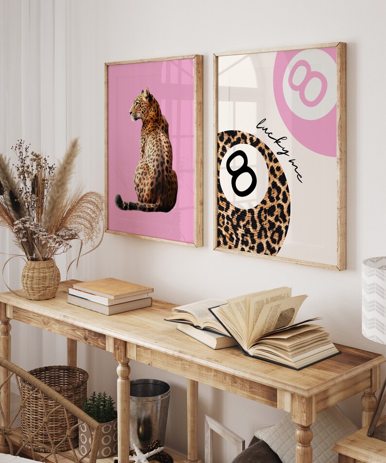 Puede incluir: Dos impresiones enmarcadas con fondo rosa. La impresi&oacute;n de la izquierda presenta un leopardo sentado sobre un fondo rosa. La impresi&oacute;n de la derecha presenta una bola de billar rosa y blanca con un dise&ntilde;o de estampado de leopardo y el texto "lucky me".