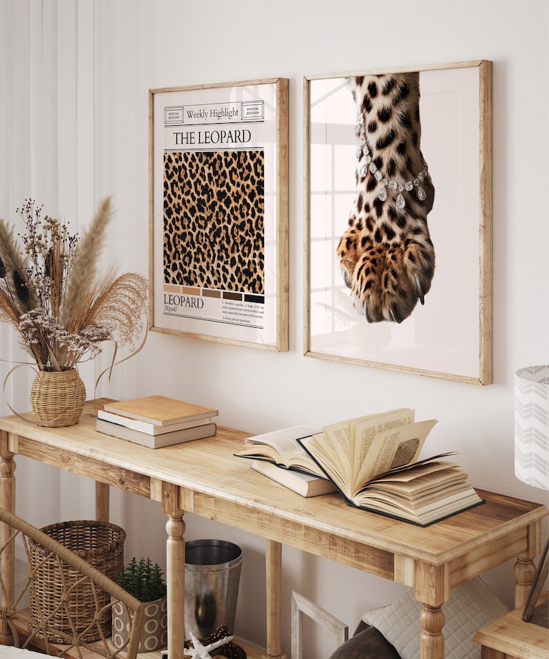 May include: Two framed prints with a leopard print theme. The print on the left features a close-up of a leopard print pattern with the text "The Leopard" and "Leopard" in a newspaper-style layout. The print on the right features a close-up of a leopard paw with a diamond bracelet around the ankle.