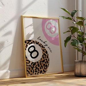 Puede incluir: Una impresi&oacute;n enmarcada con un dise&ntilde;o de bola 8 rosa y blanca y un dise&ntilde;o de bola 8 de estampado de leopardo. El texto "lucky me" est&aacute; escrito en cursiva en la impresi&oacute;n.