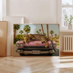 Puede incluir: Impresi&oacute;n enmarcada de un coche rosa vintage con un leopardo descansando sobre el cap&oacute;. Palmeras y un cielo azul forman el fondo. El coche tiene la matr&iacute;cula "2FLT842".