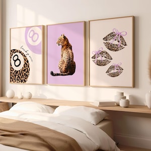 May include: Three framed art prints with a leopard print theme. One print features a leopard print eight ball with the text "lucky me". Another shows a leopard sitting on a purple background. The third print displays leopard print lips with purple bows.