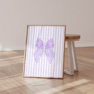 May include: A framed print with a purple bow on a white and purple striped background.