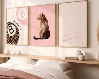 Op de afbeelding: Drie ingelijste prints met roze achtergronden. De linker print heeft een 8-ball met luipaardprint en de tekst "lucky me". De middelste print heeft een luipaard dat op zijn achterpoten zit. De rechter print heeft de tekst "Dream Big, Hustle Hard".