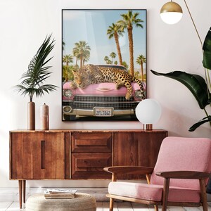 May include: A pink vintage car with a leopard lying on the bonnet. The car is parked in front of palm trees and a blue sky. The number plate reads "2FLT842".