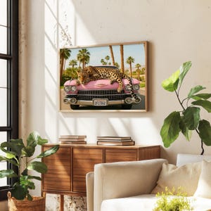 Puede incluir: Un cuadro enmarcado que muestra un coche rosa vintage con un leopardo descansando sobre el cap&oacute;. Palmeras y un cielo azul forman el fondo. La matr&iacute;cula dice "2FLT842". La obra de arte se exhibe en una habitaci&oacute;n con luz natural.