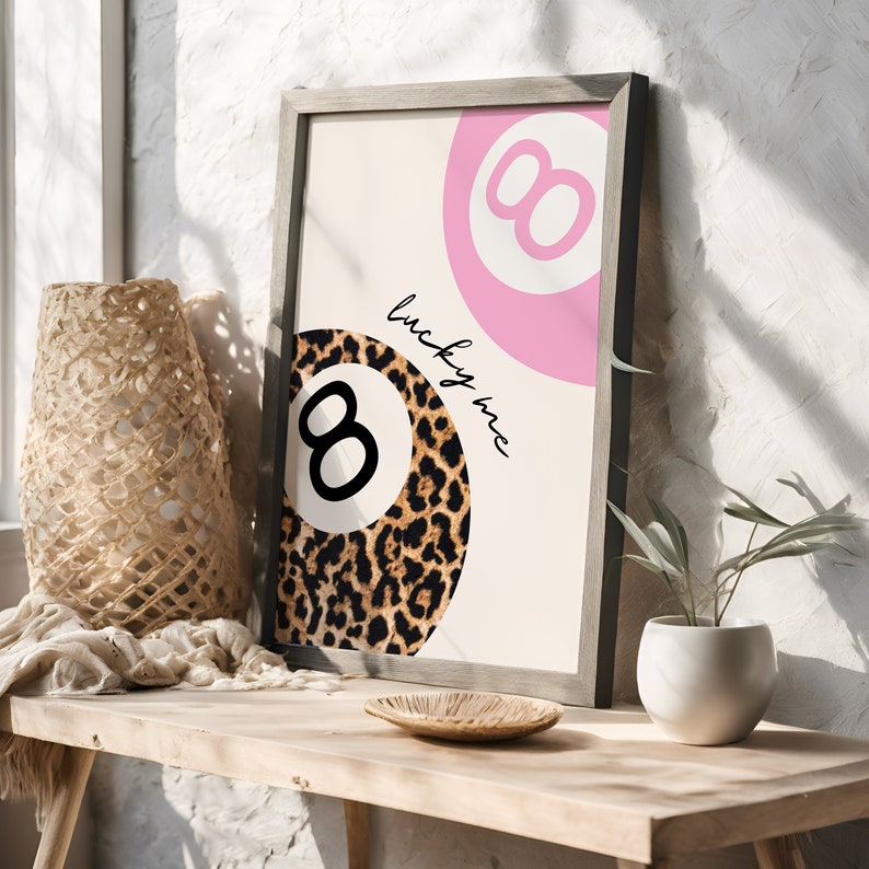 Puede incluir: Una impresi&oacute;n enmarcada con un dise&ntilde;o de bola 8 rosa y negra. La impresi&oacute;n tiene el texto "lucky me" escrito en ella.
