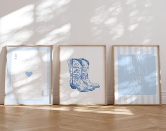 May include: Three framed prints with a light blue and white color scheme. The prints feature a playing card, a pair of cowboy boots, and the text "HOW LUCKY ARE WE." The prints are displayed on a wooden floor.