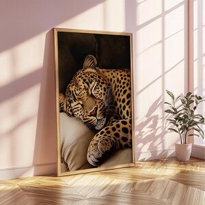 Pu&ograve; includere: Stampa artistica incorniciata raffigurante un leopardo che dorme. Il leopardo ha un mantello marrone con macchie nere e poggia la testa su un cuscino beige. L'opera d'arte &egrave; in una cornice dorata e poggia su un muro rosa.