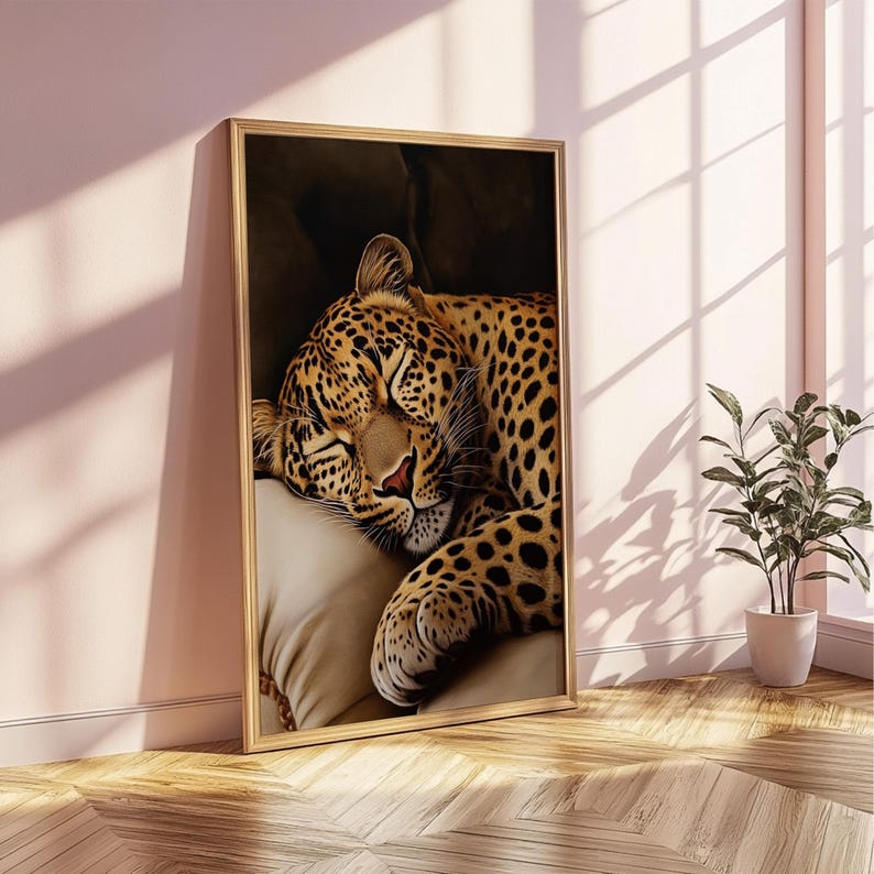 Pu&ograve; includere: Stampa artistica incorniciata raffigurante un leopardo che dorme. Il leopardo ha un mantello marrone con macchie nere e poggia la testa su un cuscino beige. L'opera d'arte &egrave; in una cornice dorata e poggia su un muro rosa.