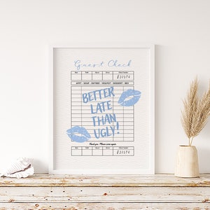 May include: A white framed print with a blue and white check design. The text "Guest Check" is at the top of the print. The check has a section for "Date", "Table", "Guests", "Server", and "Check Number". The check number is 037574. The text "APPT - SOUP - ENTREE - VEG/POT - DESSERT - BEV" is below the check number. The text "BETTER LATE THAN UGLY!" is written in blue on the check. There are two blue lips printed on the check. The text "Thank you. Please come again" is below the check. The check number 037574 is at the bottom of the print.