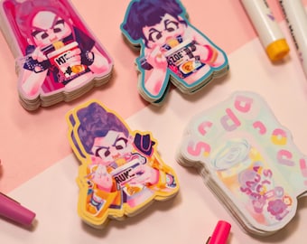 May include: A collection of colorful stickers featuring cartoon characters eating noodles. The stickers have a pink, blue, and yellow color scheme. Pens and pencils are scattered around the stickers on a pink surface.