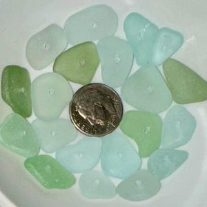 Peut inclure: Une collection de morceaux de verre de mer dans des tons de vert et de bleu. Le verre de mer est lisse et poli, avec une vari&eacute;t&eacute; de formes et de tailles. Le verre de mer est dispos&eacute; dans un bol, avec une pi&egrave;ce d'argent au centre.
