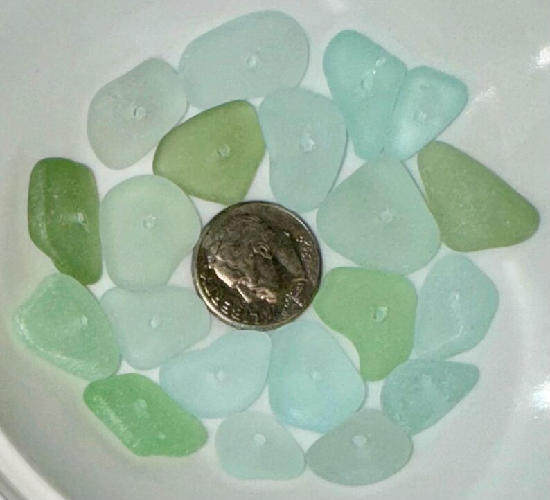 Peut inclure: Une collection de morceaux de verre de mer dans des tons de vert et de bleu. Le verre de mer est lisse et poli, avec une vari&eacute;t&eacute; de formes et de tailles. Le verre de mer est dispos&eacute; dans un bol, avec une pi&egrave;ce d'argent au centre.