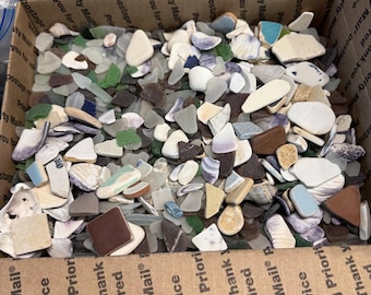 May include: A cardboard box filled with a variety of sea glass and shells. The sea glass pieces are in shades of green, blue, white, and brown. The shells are white and tan. The box has text that reads "Priority Mail Service".