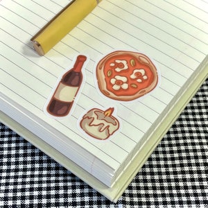 Puede incluir: Tres pegatinas en un cuaderno de l&iacute;neas: una botella de vino, una vela encendida y una pizza con flores blancas y hojas verdes.