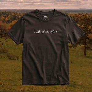 Op de afbeelding: Een donker antracietgrijs T-shirt met korte mouwen en een ronde hals, voorzien van de witte cursieve tekst 'a March sister at heart' op de borst. Het shirt heeft een standaard pasvorm met een ronde halslijn en een klein rond logo in de nek.