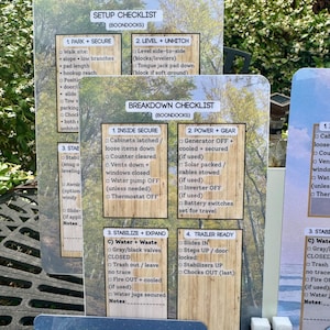 May include: A set of laminated checklists for RV setup and breakdown, featuring detailed instructions and bullet points. The cards have a wood-grain background with text in black. The checklists include sections for parking, leveling, securing, and preparing the trailer.