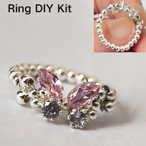 May include: A silver ring DIY kit with pink and clear stones. The ring is made of small silver beads and features two marquise-shaped pink stones and two round clear stones.