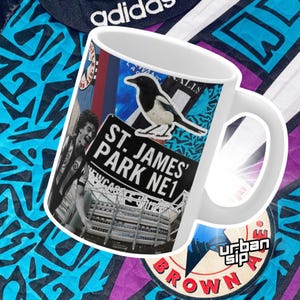 May include: White ceramic mug with a colorful collage design featuring a black and white magpie, a sign that reads "St. James' Park NE1", and a view of a stadium. The mug has a black handle.