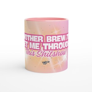 May include: A ceramic coffee mug with a pink interior and a gradient exterior of pink, orange, and yellow. The mug features the text "ANOTHER BREW TO GET ME THROUGH This Shitshow" in pink. The Urban Sip logo is at the bottom.