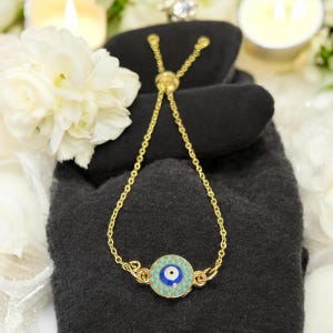 May include: A gold chain bracelet with an adjustable sliding clasp and a blue evil eye charm. The charm is surrounded by turquoise colored stones.
