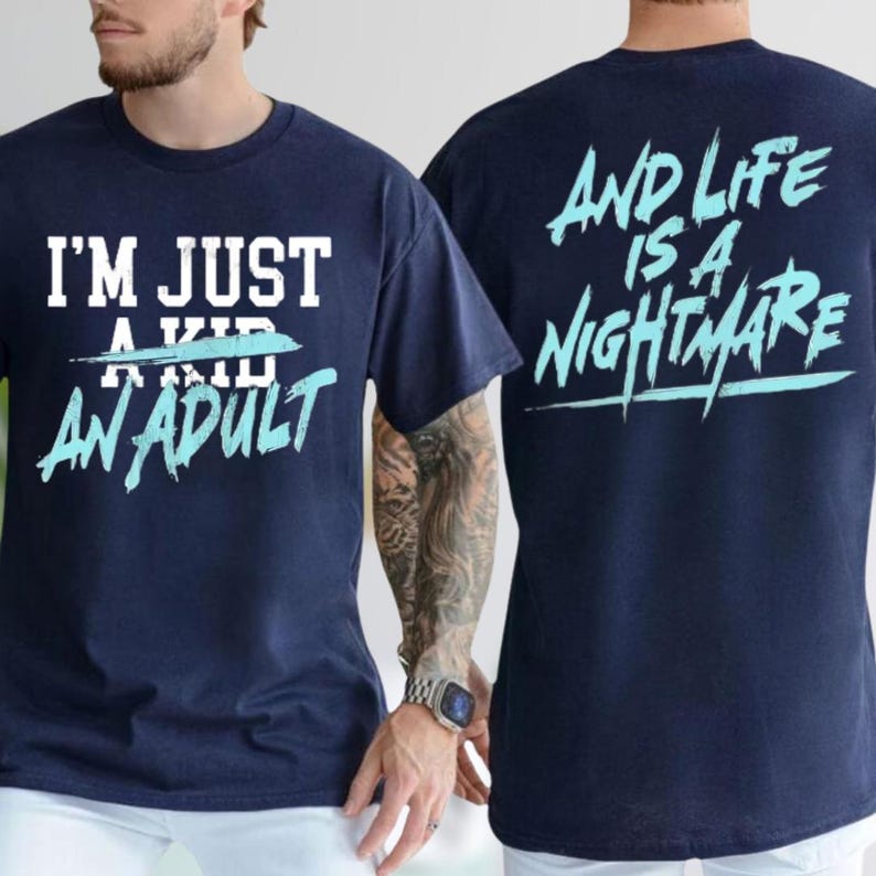 A man wearing a navy blue t-shirt with the text "I'M JUST A KID AN ADULT" printed on it, along with a tattoo on his arm.