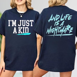 A woman wearing a navy blue t-shirt with the text "I'M JUST A KID" printed on the front and "AND LIFE IS A NIGHTMARE" printed on the back.