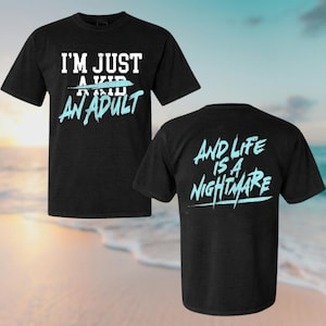 A black t-shirt with text printed on it, set against a beach scene with waves and a sunset in the background.