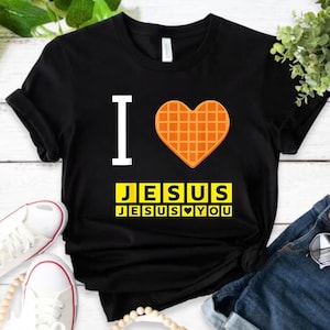 A black t-shirt with a heart-shaped waffle and the text "I ♥ JESUS JESUS YOU" printed on it, along with a pair of sneakers and a pair of jeans.