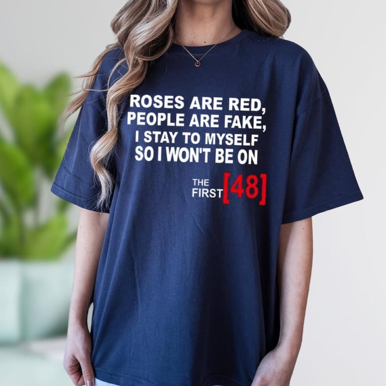 A person wearing a navy blue t-shirt with text that reads "Roses are red, people are fake, I stay to myself so I won't be on The first (481)" printed on it.
