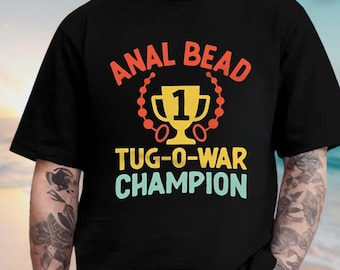 May include: Black t-shirt with the text "ANAL BEAD TUG-O-WAR CHAMPION" in orange, yellow, and teal. The design includes a trophy and a beaded necklace.
