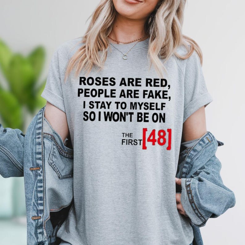 A woman wearing a gray t-shirt with text that says "Roses are red, people are fake, I stay to myself so I won't be on THE FIRST 481".