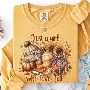 May include: A mustard yellow long-sleeve shirt featuring a graphic print with the text Just a girl who loves fall. The design includes a knit beanie, a pumpkin, a coffee drink, a football with a bow, sunflowers, and autumn leaves.