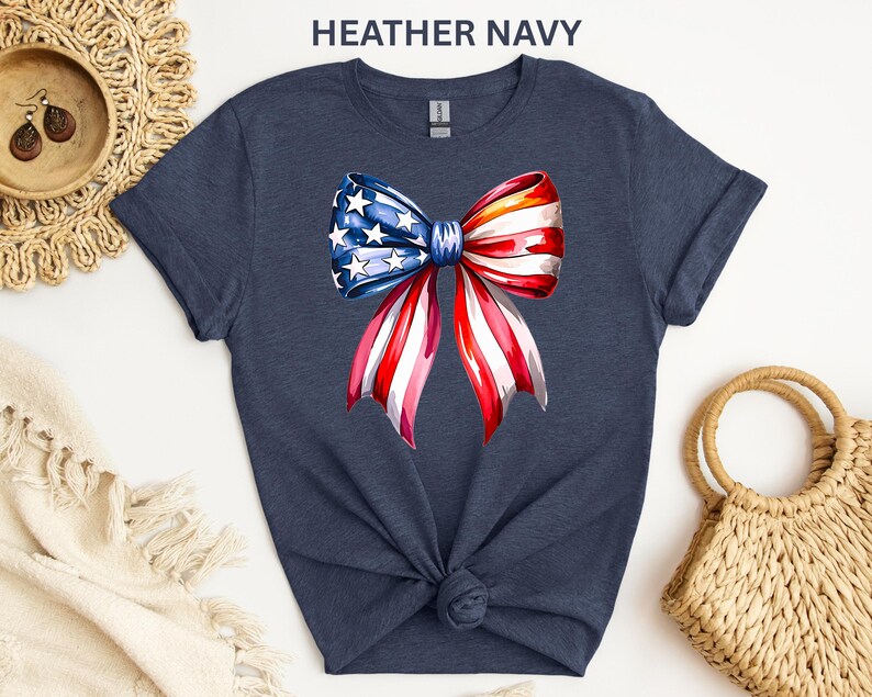 May include: Heather navy t-shirt featuring a watercolor bow design in red, white, and blue, with stars on the blue section. The shirt is knotted at the waist. The text "HEATHER NAVY" is at the top.