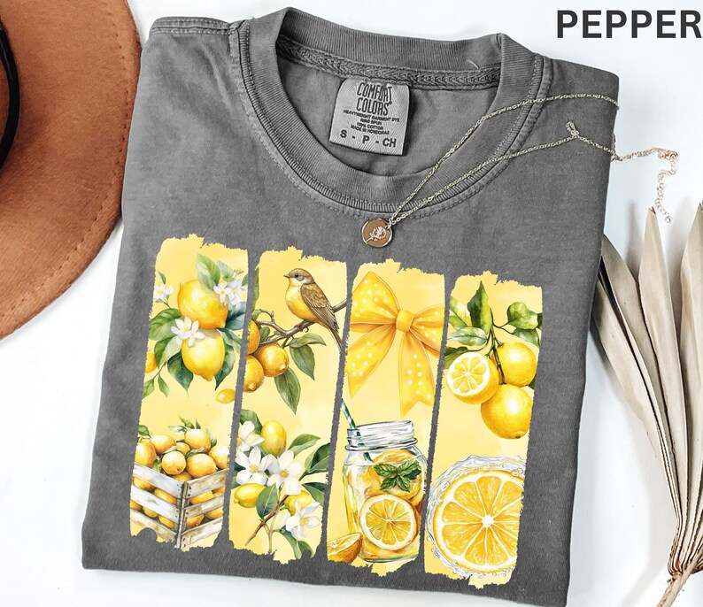 May include: A gray Comfort Colors t-shirt with a watercolor design featuring lemons, a bird, and a yellow bow. The design includes a mason jar with a lemon slice and the word "PEPPER" at the top right.