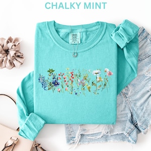 May include: A turquoise long-sleeve shirt with a floral design across the chest. The shirt is paired with denim shorts and accessories. The text "CHALKY MINT" is at the top of the image.