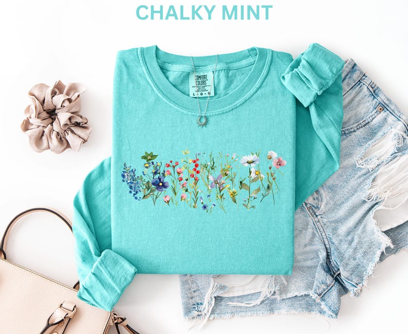 May include: A turquoise long-sleeve shirt with a floral design across the chest. The shirt is paired with denim shorts and accessories. The text "CHALKY MINT" is at the top of the image.
