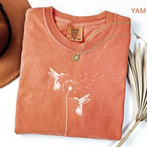 a red t-shirt with a white bird design, a brown hat, and a fan, all placed on a white surface.