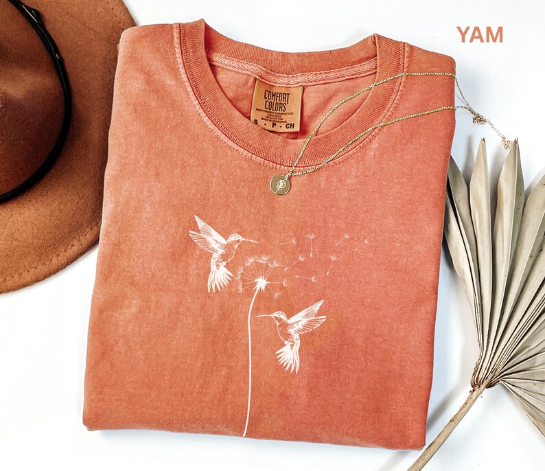 a red t-shirt with a white bird design, a brown hat, and a fan, all placed on a white surface.